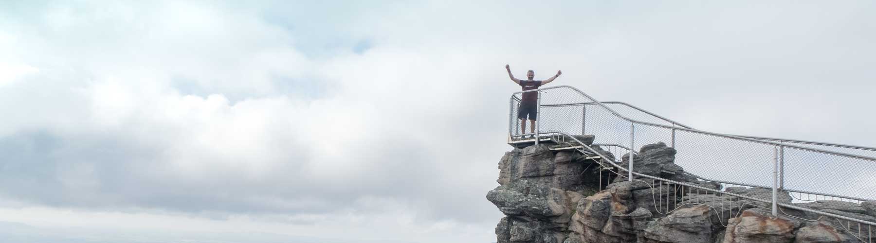 A person standing with hands in the air triumphantly atop a mountain, behind safety railing