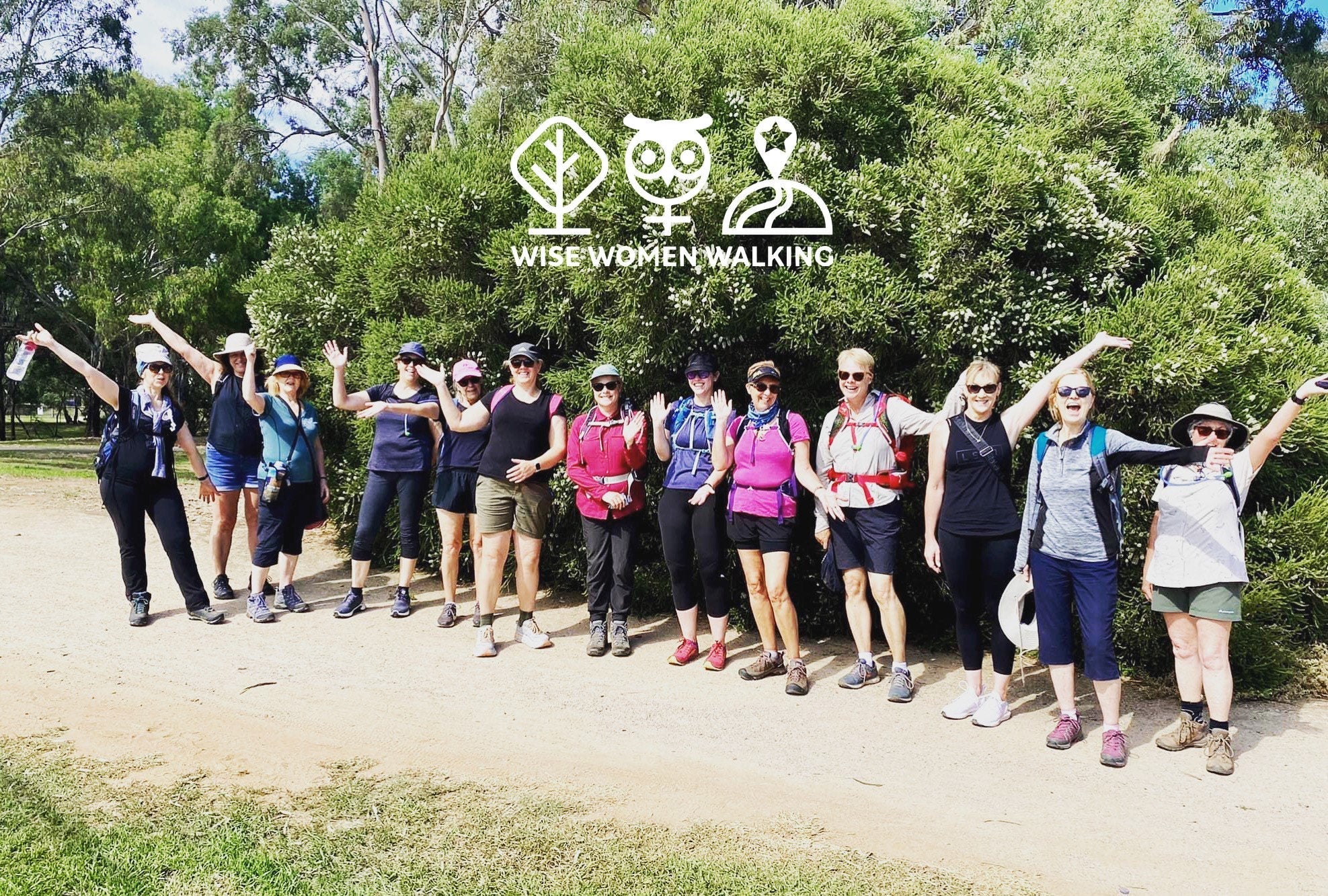 Image of a group of women in hiking gear with their arms raised in celebration, standing in front of shrubbery, text above them that reads Wise Women Walking, along with logos of a tree, an owl and symbol for female combined, and a trail.